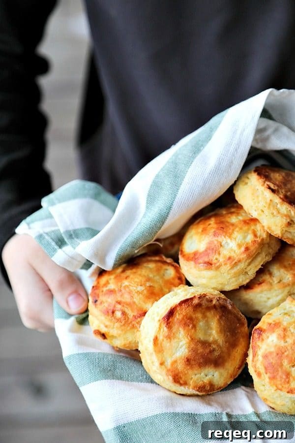 Buttermilk Biscuits: Make, Freeze, and Bake Later for Fresh Results 9 perfect flaky buttermilk biscuits in green and white towel lined bowl, held by boy in black long sleeved shirt, wooden porch