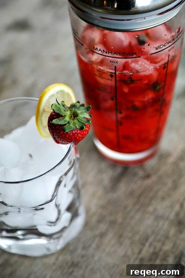 Strawberry Basil Lemonade Cocktail Recipe | Summer Boozy Drink 2 glass cocktail shaker, ice in bormioli rocco sorgente highball glass, strawberry and lemon garnish, rustic wood table