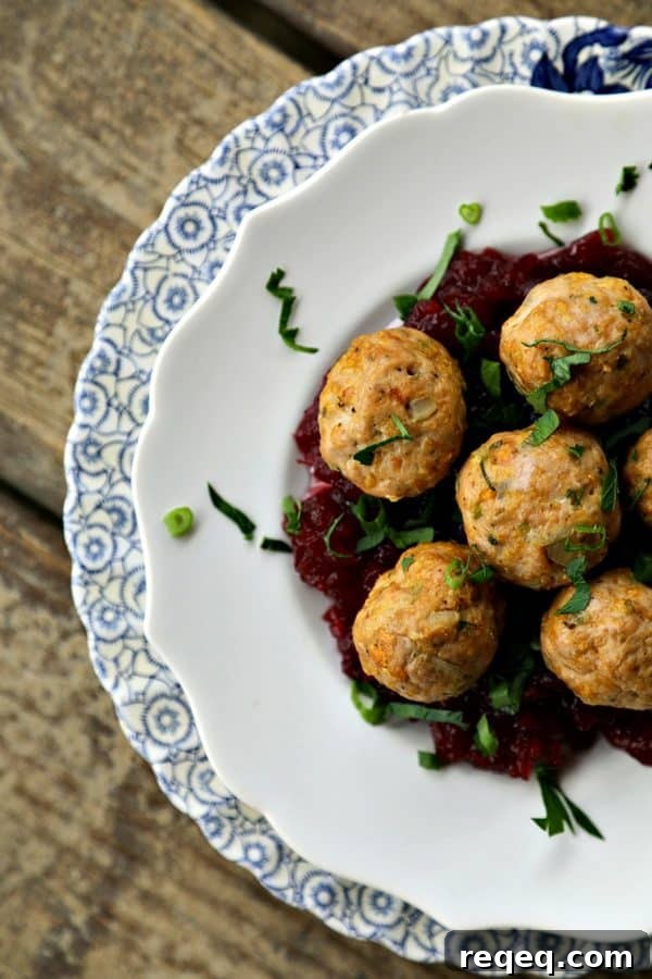 Turkey and stuffing meatballs with cranberry sauce, plated on a scalloped plate.