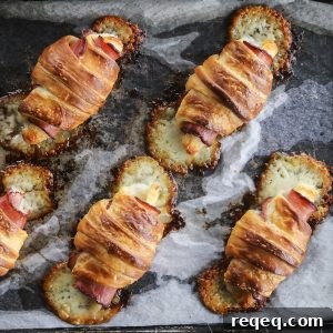 Ham & Cheese Croissants: Flaky Homemade Recipe for Breakfast 7 Ham and Cheese Croissants baked on parchment and metal sheet pan, crisp melted cheese running from ends, toasted ham, dark edges ham, pools melted cheese