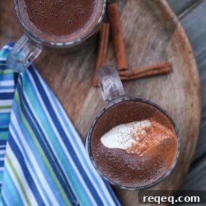 Blender made Spiced Hot Chocolate topped with cream and cinnamon, wooden tray, blue green and white towel, cinnamon sticks,