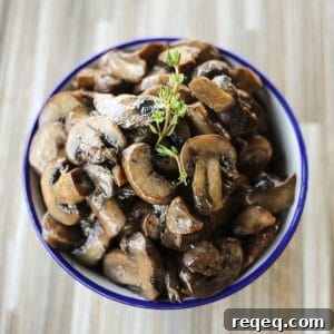 Garlic Butter Sautéed Mushrooms Recipe for Quick Flavor 5 blue edged, white ceramic bowl, wooden tile background, simple garlic butter sauteed mushrooms, sprig of fresh thyme
