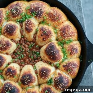 Cheeseburger Bombs Skillet with Baked Beans and Melty Cheese 4 Cheeseburger Bombs Baked Bean Skillet, sesame topped rolls stuffed with meatballs, arranged in circles around baked beans, cast iron skillet, sliced green onions