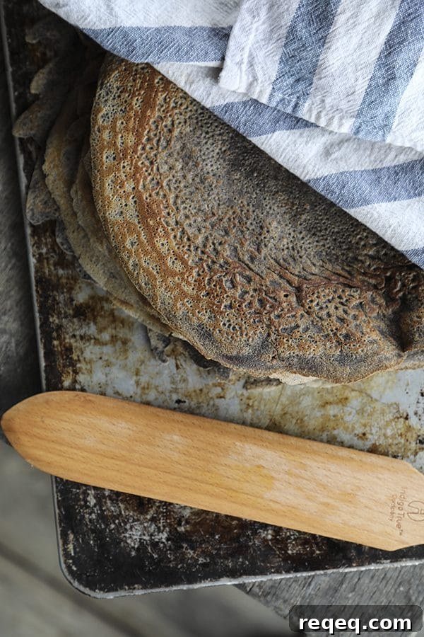 Buckwheat Crepes Recipe – Naturally Gluten Free Pancakes 3 Pure buckwheat crepes on an antique cookie sheet under a blue and white towel, wooden crepe turner