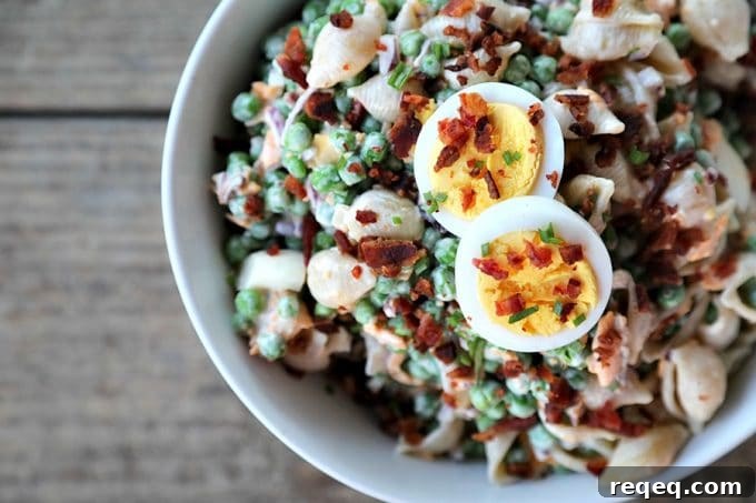 Creamy Bacon and Pea Pasta Salad with Tangy Dressing 2 bacon pea pasta salad in white bowl with hard boiled eggs, bacon bits, rustic wood table