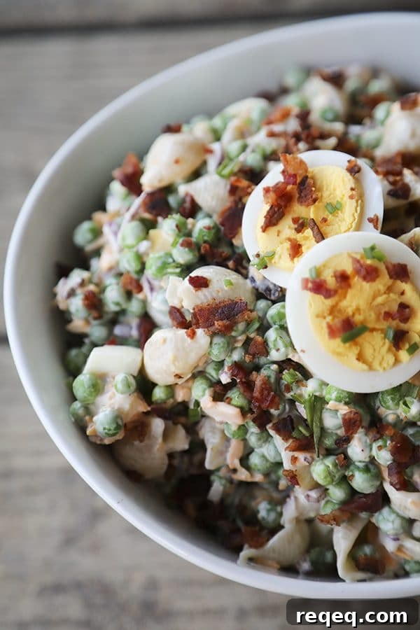 Creamy Bacon and Pea Pasta Salad with Tangy Dressing 3 bacon pea pasta salad in white bowl with hard boiled eggs, bacon bits, rustic wood table