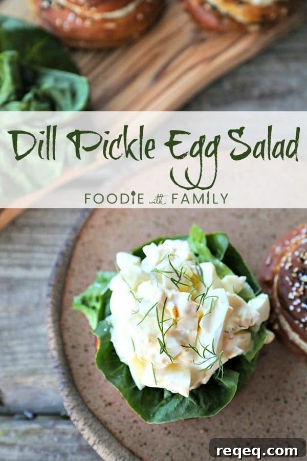 Dill Pickle Egg Salad is classic creamy egg salad packed with cubes of crispy dill pickles, and fresh dill. Served on a pretzel roll it's heaven! Dill Pickle Egg Salad with fresh dill on lettuce and soft pretzel roll, speckled brown pottery plate with rough edge, wooden cutting board with rolls and lettuce, rustic wooden table.