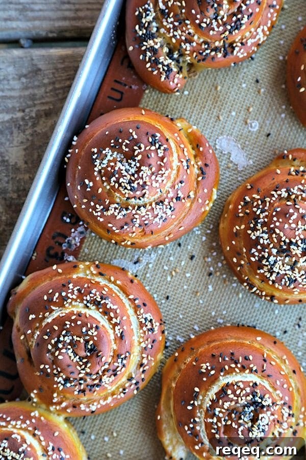 The most perfect soft pretzel rolls for sandwiches. Tender yet chewy, and substantial enough to hold up to any fillings. Topped with a delightful combination of sesame seeds and pretzel salt. Soft pretzel rolls for sandwiches, silpat, half sheet pan, rustic wood table, sesame seeds, pretzel salt