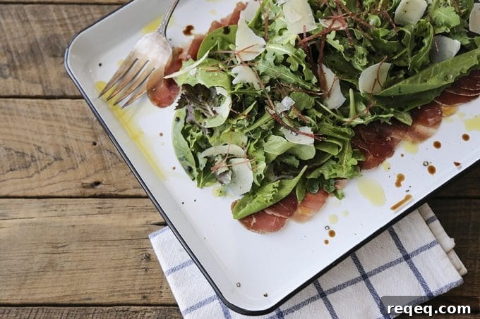 Bresaola and Parmesan Salad with Arugula and Lemon Dressing 2 Bresaola Parmesan Salad on white quarter sheet pan with cobalt blue rim, blue and white tea towel, antique fork, rustic wood tabletop