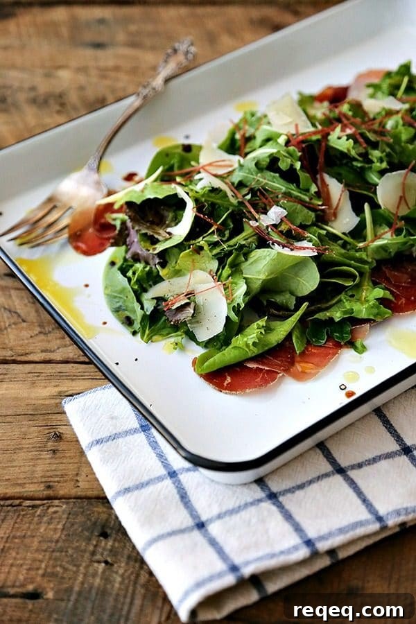 Bresaola and Parmesan Salad with Arugula and Lemon Dressing 3 Bresaola Parmesan Salad on white quarter sheet pan with cobalt blue rim, blue and white tea towel, antique fork, rustic wood tabletop