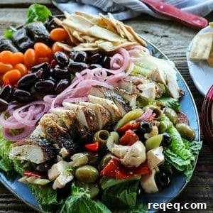 Greek Salad with lemon garlic chicken, marinated olive salad, quick pickled red onions, crumbled feta cheese, garlic stuffed kalamata olives, tiny grape tomatoes, stuffed grape leaves, Greek salad dressing, pita chips as croutons, and a hearty dollop of hummus.