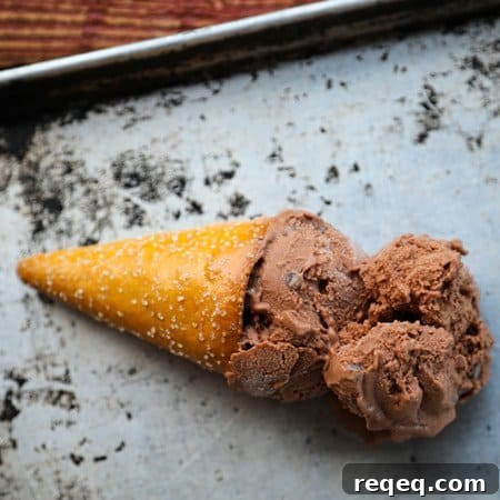 Two scoops of vegan dairy free chocolate ice cream in a pretzel cone on an antique sheet pan.