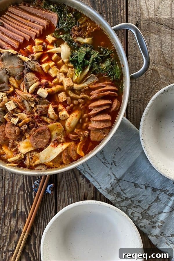 Budae Jjigae (Korean Army Stew): Spicy Sausage Hot Pot 2 Korean Army Stew in a stainelss steel pan with two empty bowls, chopsticks, and a blue linen.