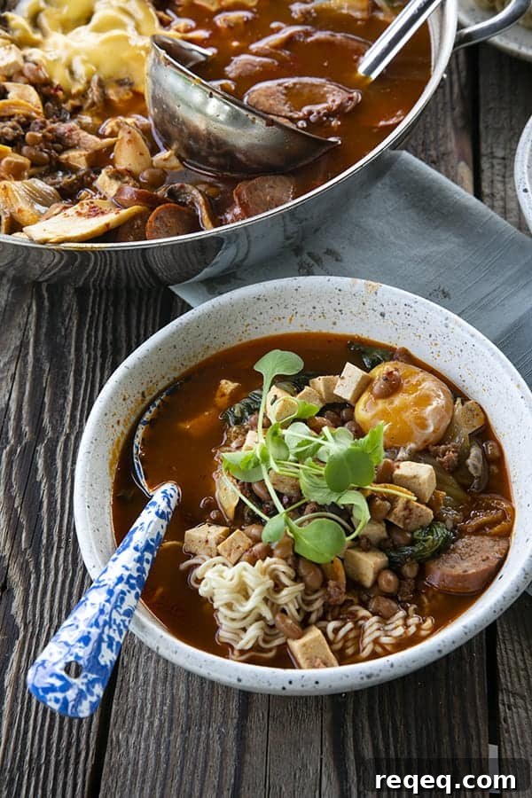 Budae Jjigae (Korean Army Stew): Spicy Sausage Hot Pot 6 Korean Army Stew or Budae Jjigae in a white bowl with an egg yolk and a blue enamel spoon.
