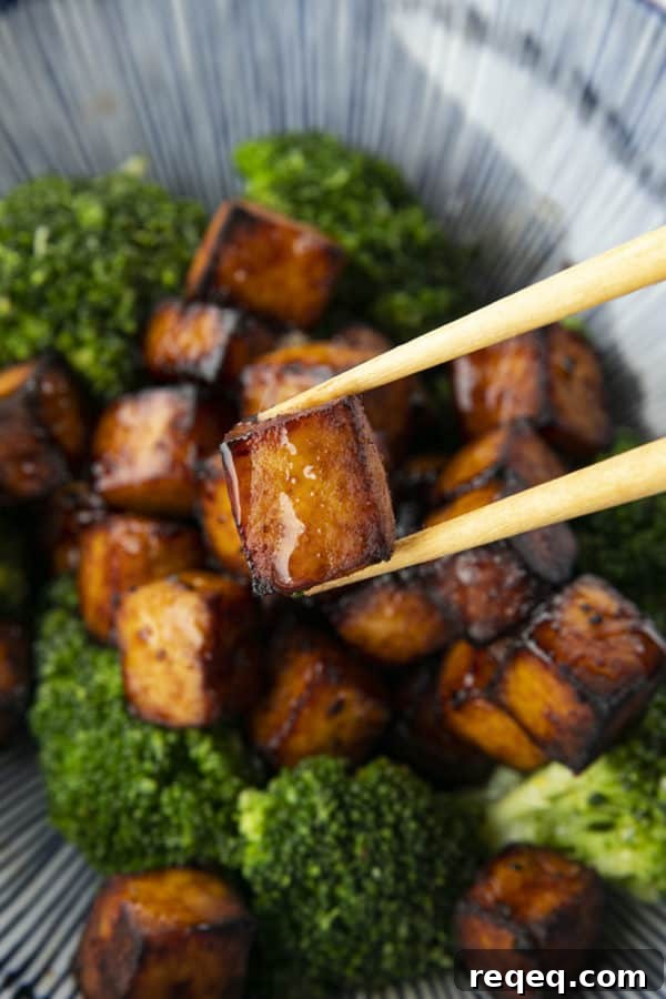 Honey Sriracha Crispy Tofu in the Air Fryer: Sticky & Crunchy 5 Crispy, golden brown cubes of air fryer tofu served with a drizzle of honey and broccoli on a blue and white striped oblong bowl.