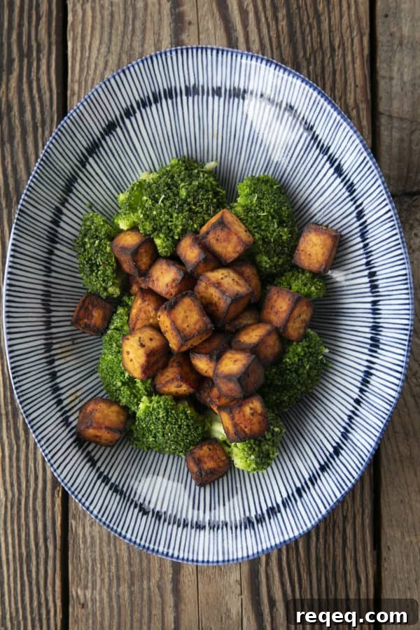 Honey Sriracha Crispy Tofu in the Air Fryer: Sticky & Crunchy 6 Crispy, golden brown cubes of air fryer tofu served with a drizzle of honey and broccoli on a blue and white striped oblong bowl.