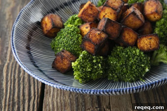 Honey Sriracha Crispy Tofu in the Air Fryer: Sticky & Crunchy 7 Crispy, golden brown cubes of air fryer tofu served with a drizzle of honey and broccoli on a blue and white striped oblong bowl.