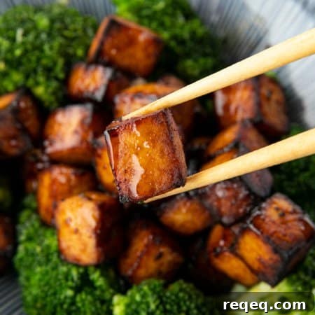 Honey Sriracha Crispy Tofu in the Air Fryer: Sticky & Crunchy 8 Crispy, golden brown cubes of air fryer tofu served with a drizzle of honey and broccoli on a blue and white striped oblong bowl.