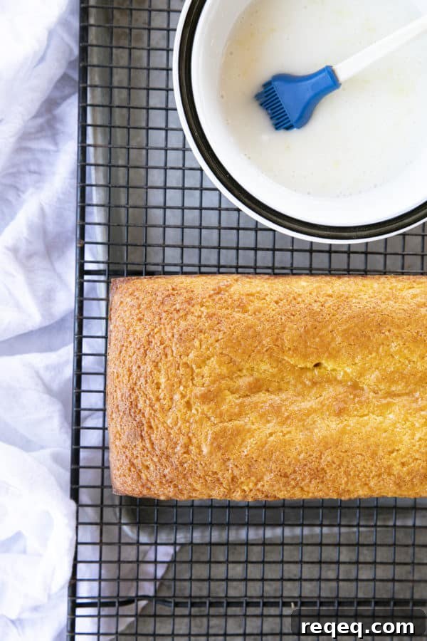 Classic French Yogurt Cake Recipe for Moist, Homemade Dessert 4 Glazing a French Grandma Lemon Yogurt Cake on a black cooling rack over a pan.