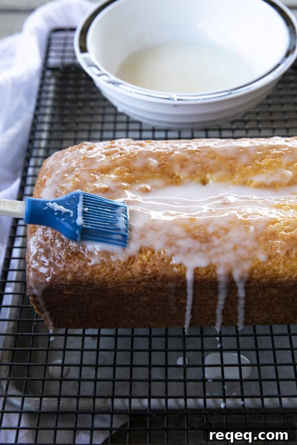 Classic French Yogurt Cake Recipe for Moist, Homemade Dessert 7 Glazing a French Grandma Lemon Yogurt Cake on a black cooling rack over a pan.