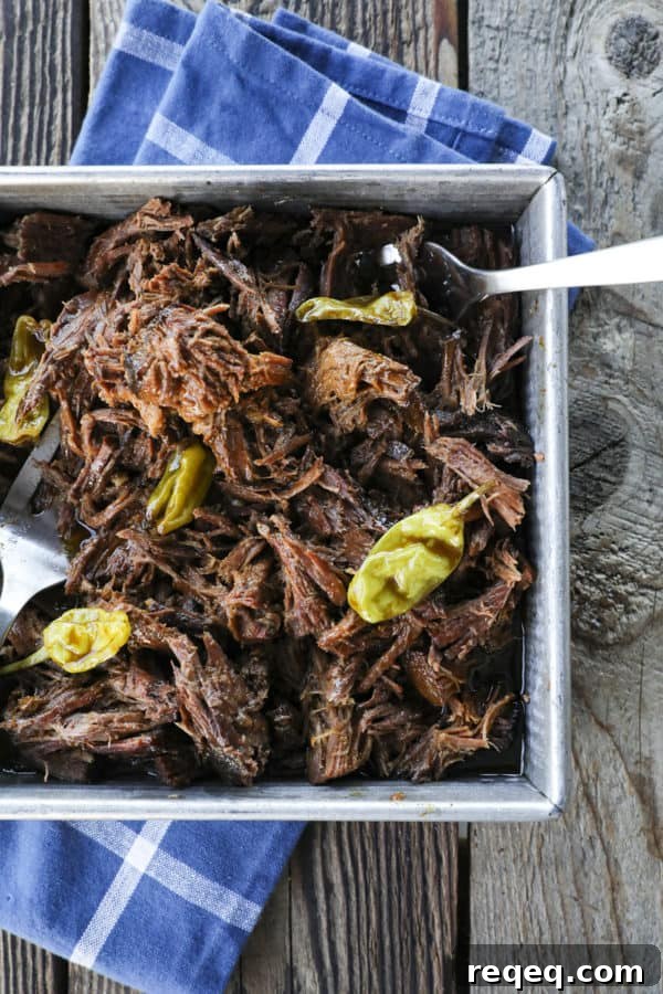Mississippi Pot Roast Slow Cooker Recipe: Tender, Flavorful Roast 2 Shredded Crock Pot Mississippi Pot Roast in a square metal pan with whole pepperoncini and meat forks on a blue linen and wooden table.