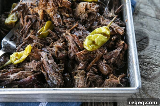 Mississippi Pot Roast Slow Cooker Recipe: Tender, Flavorful Roast 3 Shredded Crock Pot Mississippi Pot Roast in a square metal pan with whole pepperoncini and meat forks on a blue linen and wooden table.