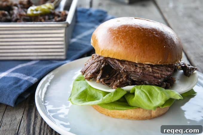 Mississippi Pot Roast Slow Cooker Recipe: Tender, Flavorful Roast 5 Shredded Crock Pot Mississippi Pot Roast served on a sandwich roll with provolone cheese and butter lettuce on a white plate with a blue linen and wooden table.