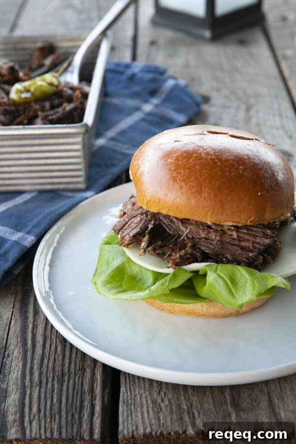 Mississippi Pot Roast Slow Cooker Recipe: Tender, Flavorful Roast 6 Shredded Crock Pot Mississippi Pot Roast served on a sandwich roll with provolone cheese and butter lettuce on a white plate with a blue linen and wooden table.