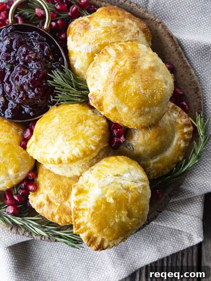 Bite sized baked brie in puff pastry with rosemary, pomegranate seeds, and sweet and spicy cranberry sauce.