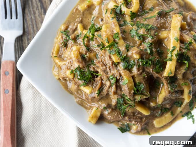 Slow Cooker Beef and Noodles Recipe for Comforting Weeknight Meals 3 crock pot beef and noodles in a white square bowl on linens