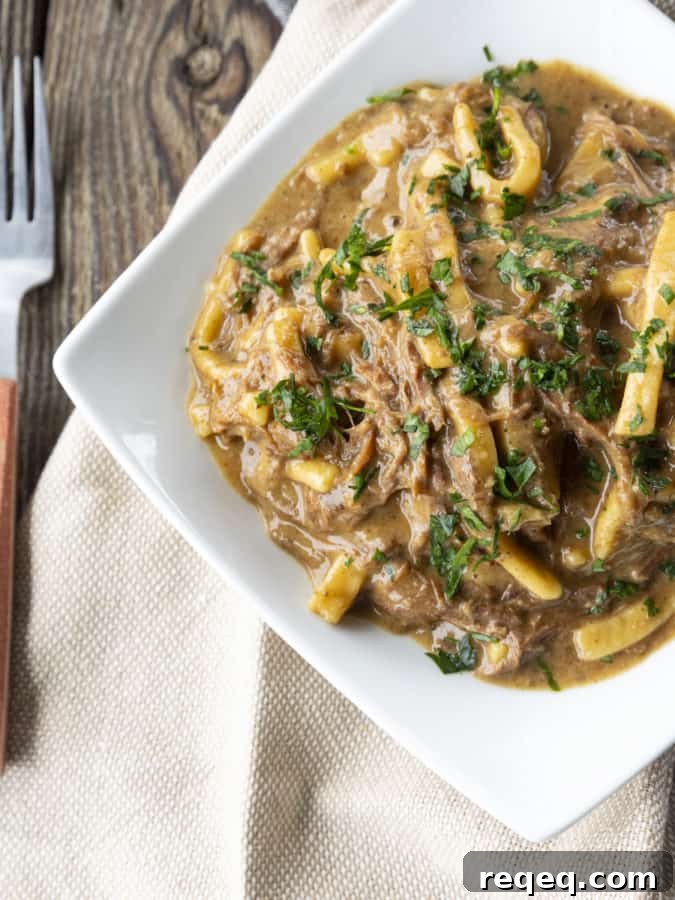 Slow Cooker Beef and Noodles Recipe for Comforting Weeknight Meals 4 crock pot beef and noodles in a white square bowl on linens