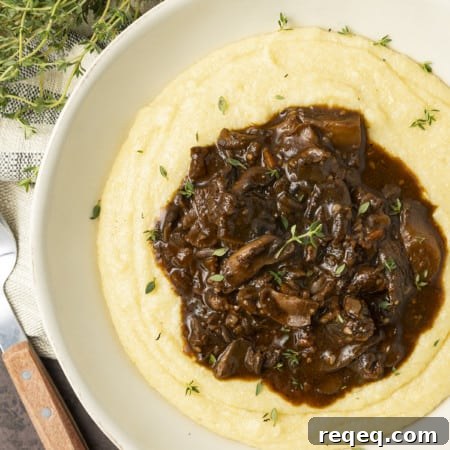 Mushroom stew over polenta in a pottery bowl with thyme nearby.