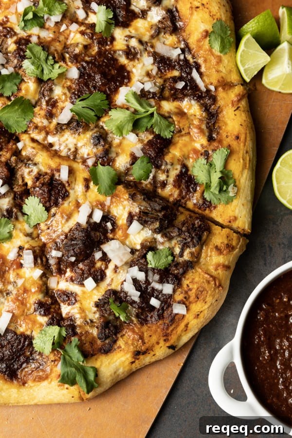 Birria Pizza: Chewy crust topped with tender shredded birria beef, smoky birria stew, loads of melted cheese, chopped sweet onion, fresh cilantro, a squeeze of fresh lime, and a bowl of red chile sauce for dipping.