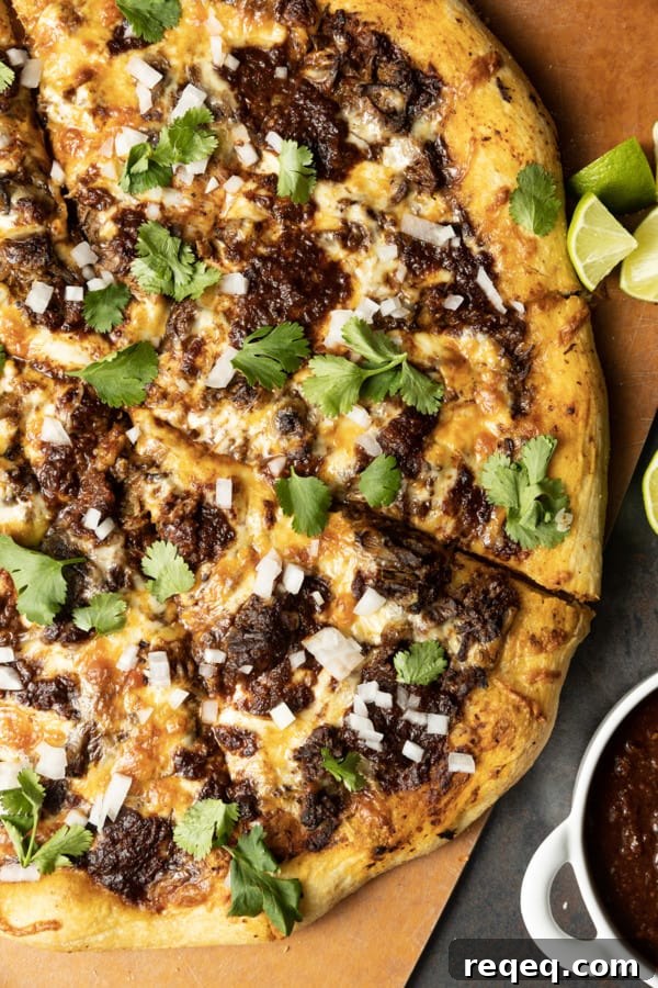 Birria Pizza: Chewy crust topped with tender shredded birria beef, smoky birria stew, loads of melted cheese, chopped sweet onion, fresh cilantro, a squeeze of fresh lime, and a bowl of red chile sauce for dipping.