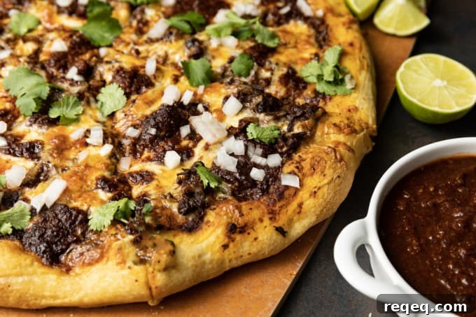 Birria Pizza: Chewy crust topped with tender shredded birria beef, smoky birria stew, loads of melted cheese, chopped sweet onion, fresh cilantro, a squeeze of fresh lime, and a bowl of red chile sauce for dipping.