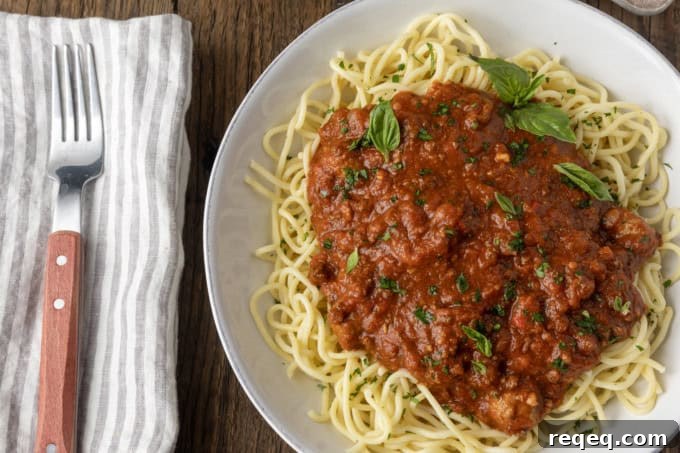 Slow-Cooker Spaghetti Sauce Recipe for Rich, Hands-Off Flavor 2 spaghetti sauce on spagetti on a plate topped by fresh herbs with a napkin and fork on the left.