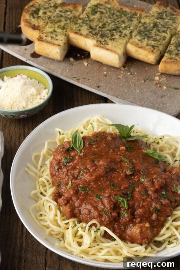 Slow-Cooker Spaghetti Sauce Recipe for Rich, Hands-Off Flavor 4 spaghetti sauce on spagetti on a plate topped by fresh herbs with a napkin and fork on the left.