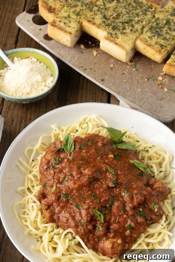 Slow-Cooker Spaghetti Sauce Recipe for Rich, Hands-Off Flavor 6 spaghetti sauce on spagetti on a plate topped by fresh herbs with a napkin and fork on the left and garlic bread on a cutting board above.
