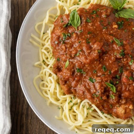 Slow-Cooker Spaghetti Sauce Recipe for Rich, Hands-Off Flavor 7 spaghetti sauce on spagetti on a plate topped by fresh herbs with a napkin and fork on the left.