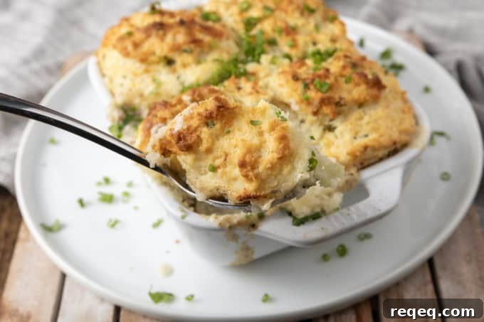 Savory Sausage Gravy Breakfast Casserole 2 small white casserole dish filled with sausage gravy and topped with buttermilk biscuit crust on top of a plate with a spoon in it.