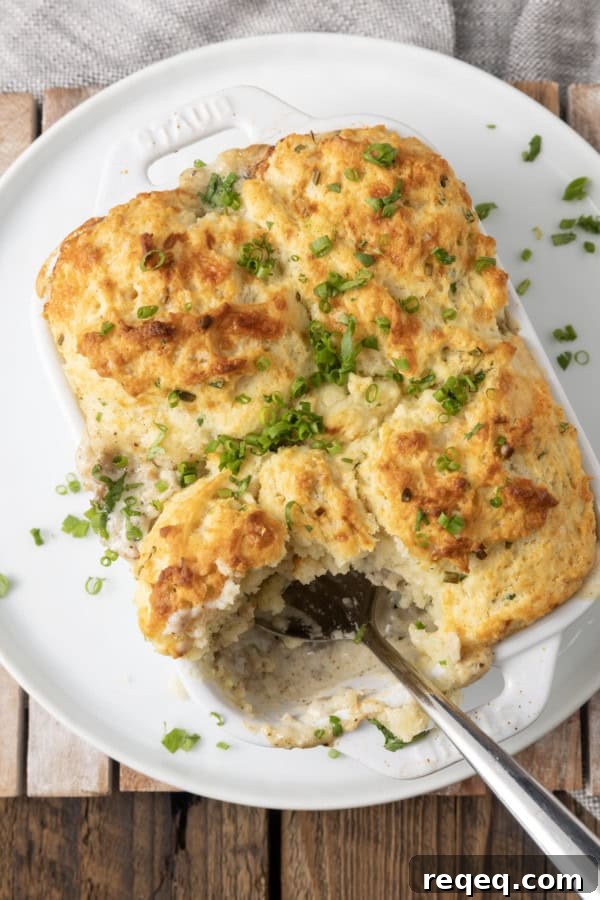 Savory Sausage Gravy Breakfast Casserole 3 small white casserole dish filled with sausage gravy and topped with buttermilk biscuit crust on top of a plate with a spoon in it.