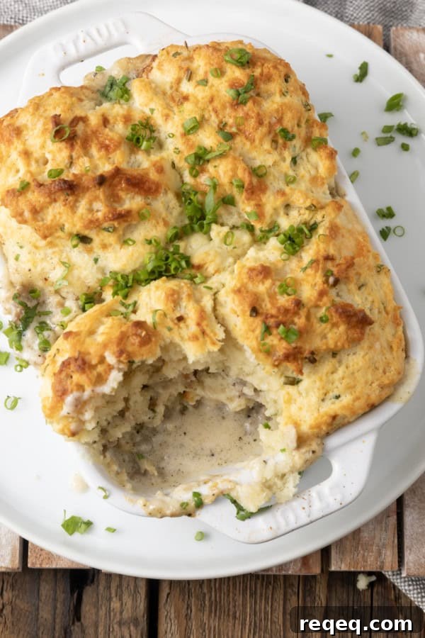 Savory Sausage Gravy Breakfast Casserole 4 small white casserole dish filled with sausage gravy and topped with buttermilk biscuit crust on top of a plate with a scoop out of it