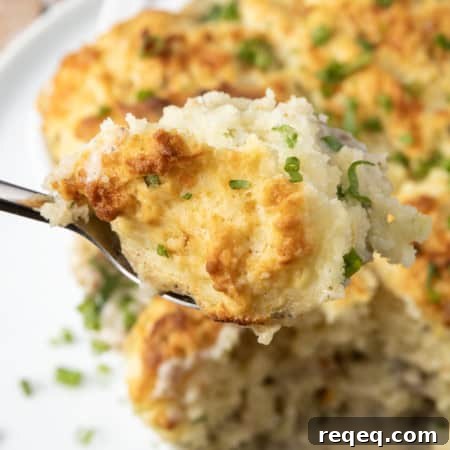 Savory Sausage Gravy Breakfast Casserole 7 small white casserole dish filled with sausage gravy and topped with buttermilk biscuit crust on top of a plate with a spoon in it.