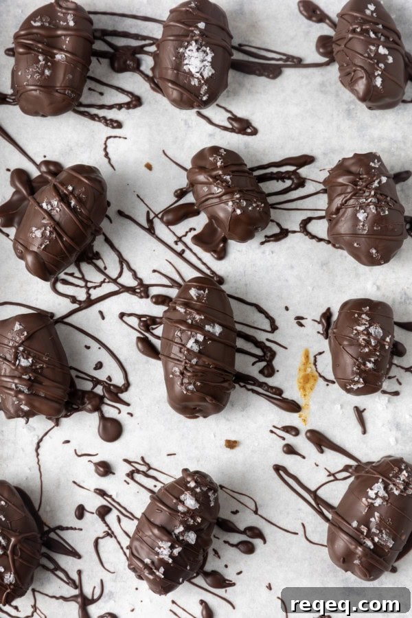 Chocolate-Covered Dates: Simple Recipe for Decadent Treats 3 chocolate covered almond stuffed dates with sea salt on parchment lined sheet pan