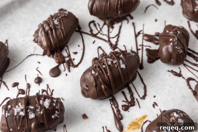 Chocolate-Covered Dates: Simple Recipe for Decadent Treats 4 chocolate covered almond stuffed dates with sea salt on parchment lined sheet pan