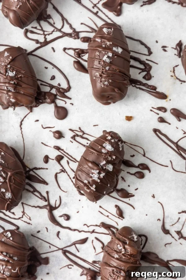 Chocolate-Covered Dates: Simple Recipe for Decadent Treats 6 chocolate covered almond stuffed dates with sea salt on parchment lined sheet pan