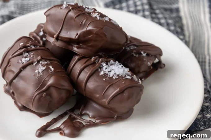 Chocolate-Covered Dates: Simple Recipe for Decadent Treats 7 almond butter stuffed medjool dates covered in chocolate and sprinkled with sea salt on small white plates with a blue and white linen
