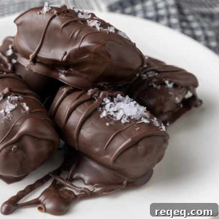 almond butter stuffed medjool dates covered in chocolate and sprinkled with sea salt on small white plates with a blue and white linen