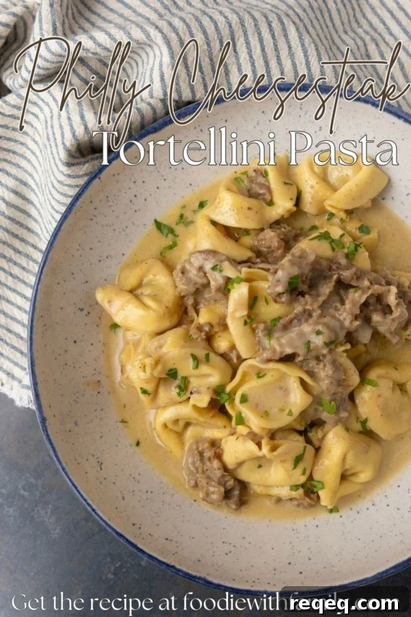 Philly cheesesteak tortellini in rich provolone sauce garnished with chopped parsley in a blue rimmed speckled bowl on a table with a blue and white striped linen with text overlay describing the photo