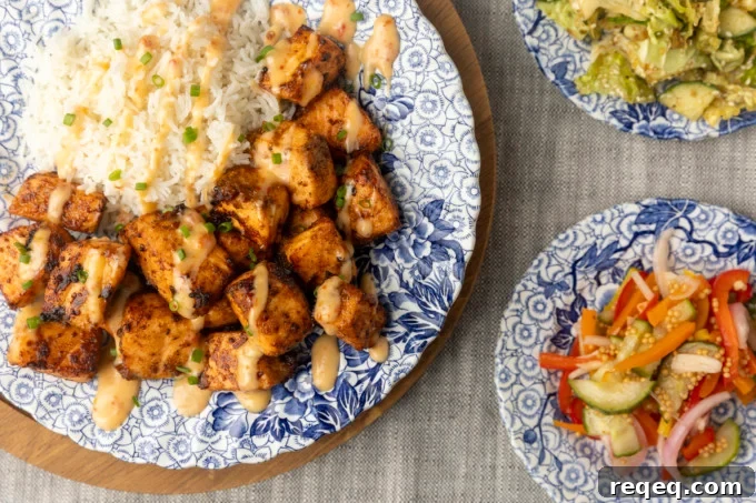Crispy Bang Bang Salmon Bites Recipe for Spicy Sweet Salmon Bites 2 crispy air fryer bang bang salmon bites drizzled with sauce served with ice on a blue and white floral plate and two smaller blue and white plates with Japanese cabbage salad and pickled pepper salad